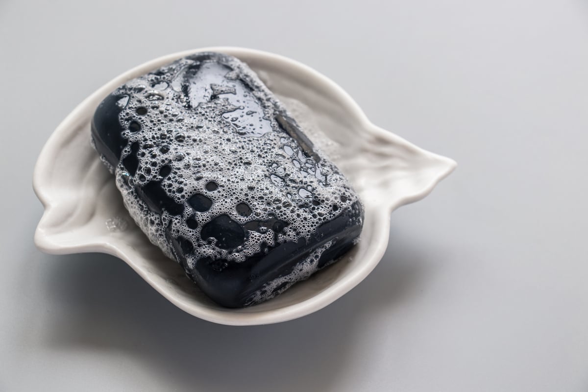 Close-up soap. Black soap bar and foam in the soap dish on a grey background. Hand made soap. For protect, health.